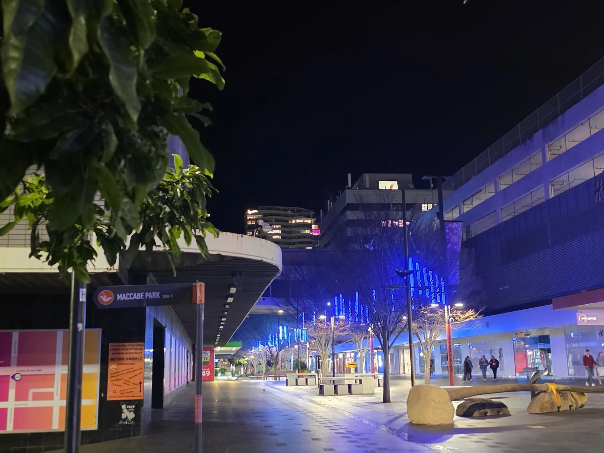 Crown Street Mall in Wollongong at night, lit shopfronts and street trees along the paving