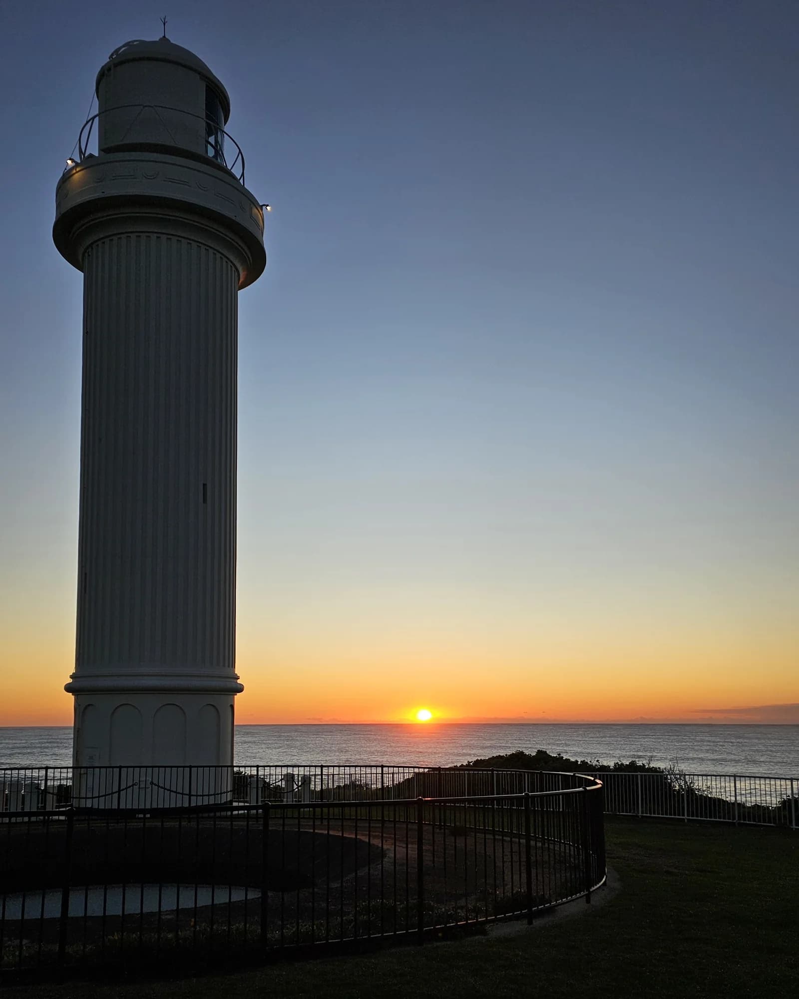 Flagstaff Point Lighthouse silhouetted against the sunrise, the sun sitting just above the ocean