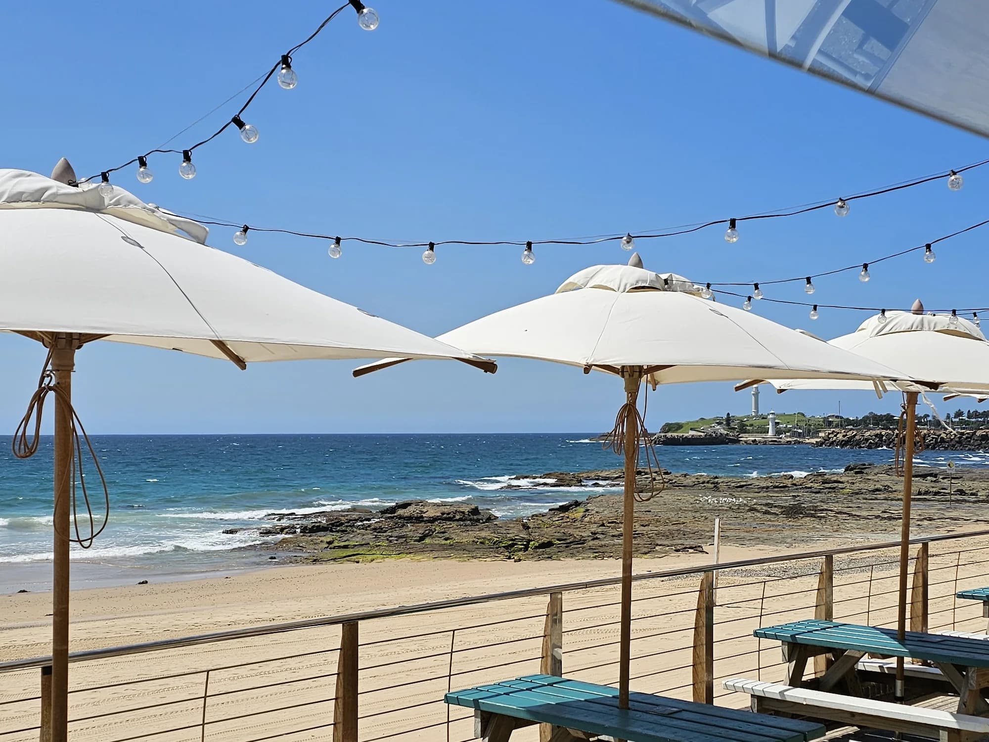 Umbrellas and picnic tables on the North Beach Pavilion deck, looking over North Wollongong Beach to the lighthouse