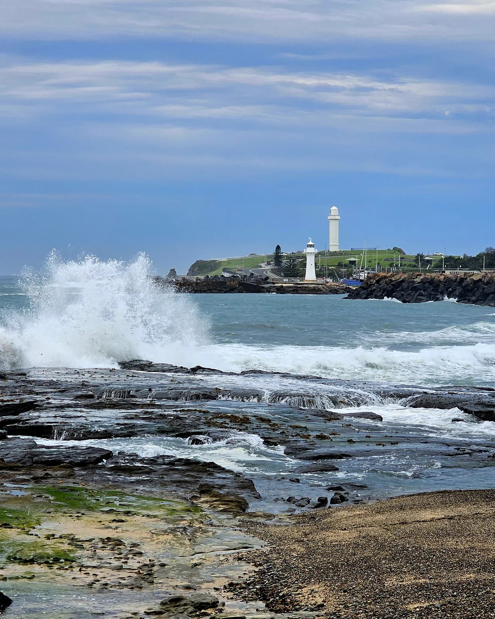 Waves breaking on the rock shelf with Flagstaff Point Lighthouse on the headland