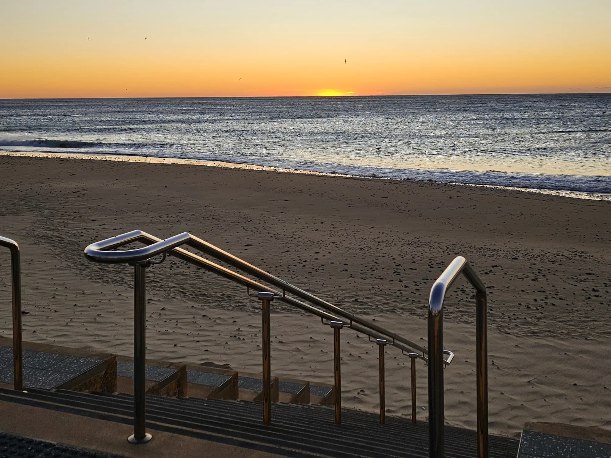 Steps and rails leading down to North Wollongong Beach at sunrise, the sun on the horizon