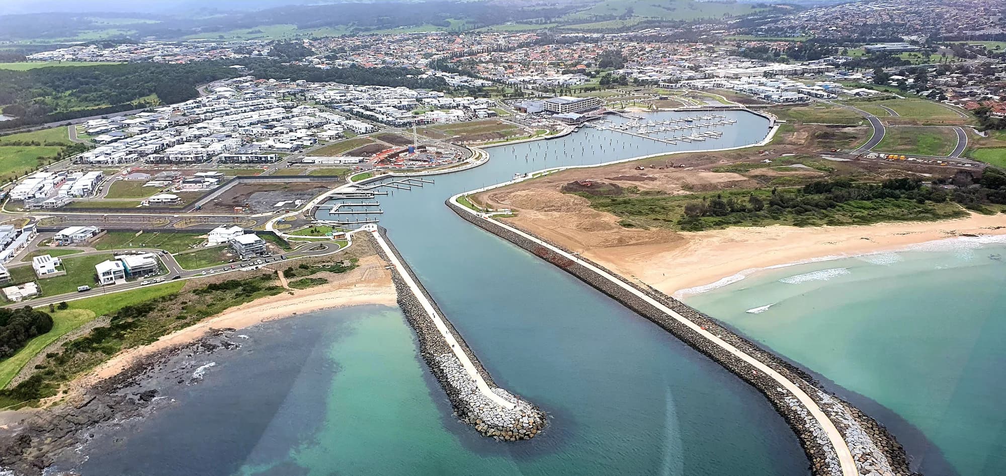 Shell Cove's new harbour from the air, its twin breakwalls opening onto turquoise water and the beach