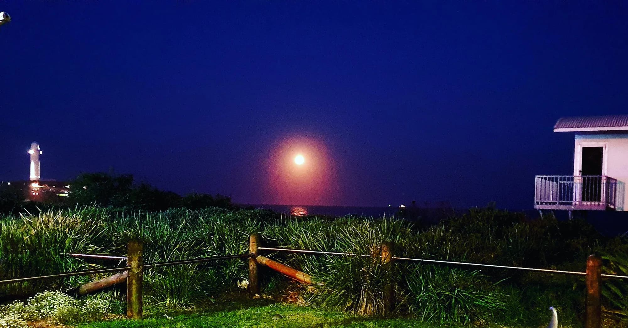 A full moon rising over the sea beside Flagstaff Point Lighthouse at night