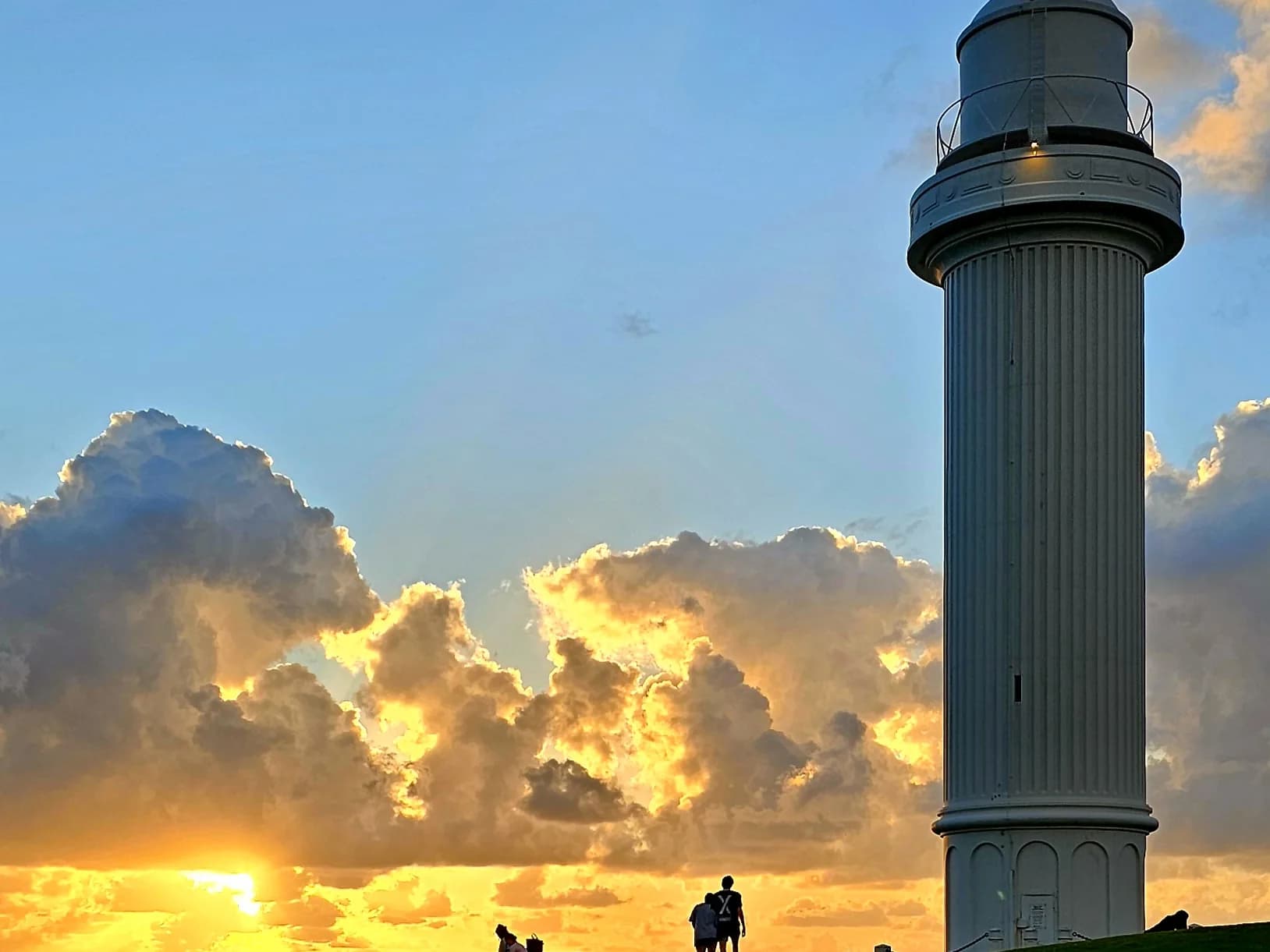 Sunrise clouds glowing behind Flagstaff Point Lighthouse on the headland above the harbour