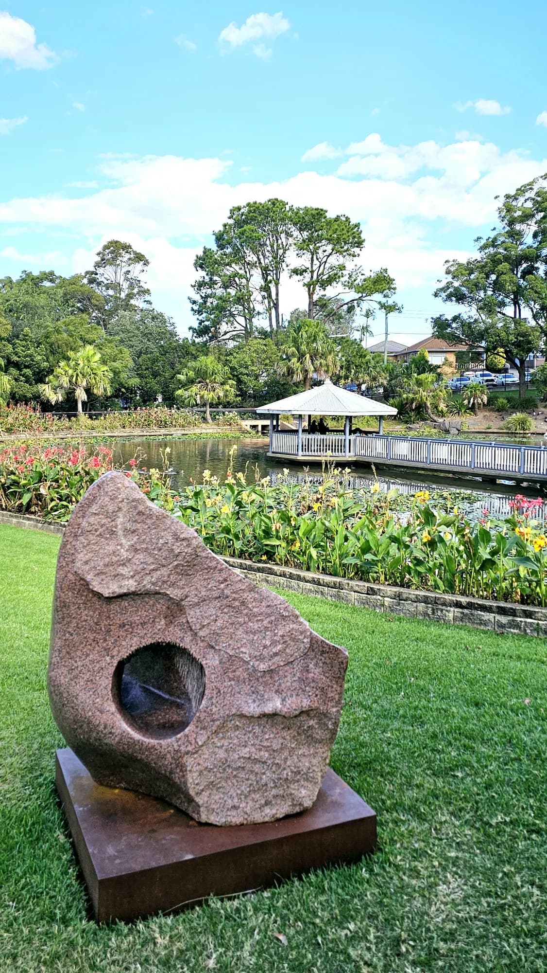 A granite sculpture on the lawn above the flower beds and pond at Wollongong Botanic Garden